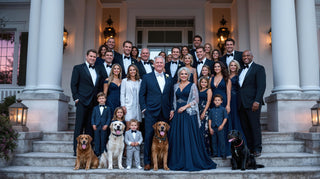 Large family gathering with adults, children, and dogs on a staircase in front of a grand building.
