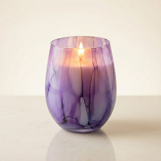 Enigmatic Bloom Feng Shui wood element luxury candle lit with glowing flame in hand-painted purple marbled glass vessel