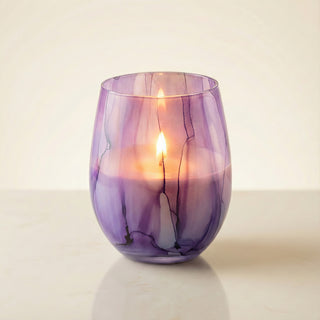 Enigmatic Bloom Feng Shui wood element luxury candle burning with warm golden flame in hand-painted purple marbled glass